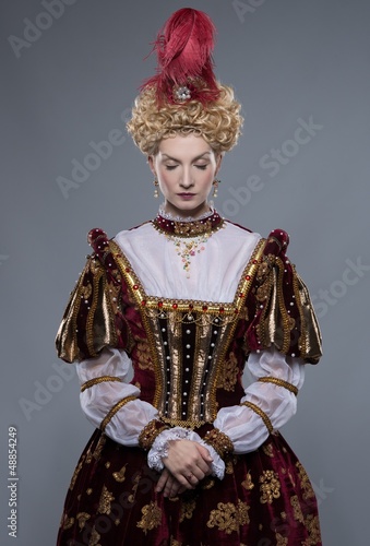 Photo: Haughty queen in royal dress isolated on grey Haughty queen in royal dress isolated on grey