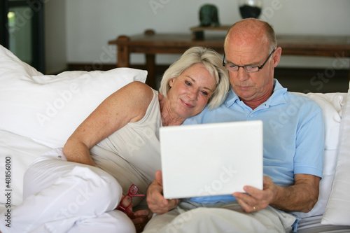 Photo: Middle-aged couple sat on sofa with laptop Middle-aged couple sat on sofa with laptop