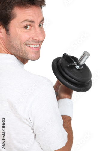 Photo: Smiling man looking over his shoulder holding dumbbell Smiling man looking over his shoulder holding dumbbell