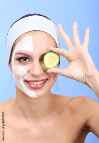 Photo: Young woman with clay facial mask, on blue background Young woman with clay facial mask, on blue background