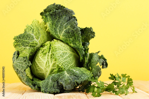 Photo: Fresh savoy cabbage on wooden table on yellow background Fresh savoy cabbage on wooden table on yellow background