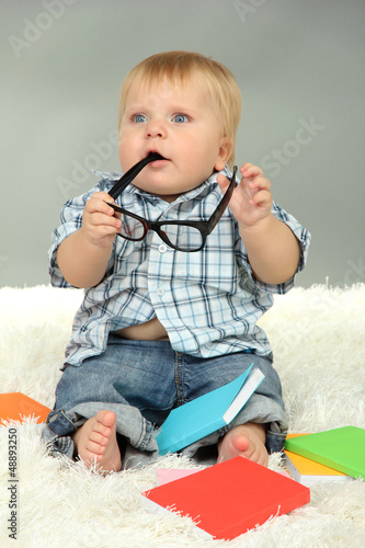 Photo: Little boy with multicolor books, on white carpet Little boy with multicolor books, on white carpet