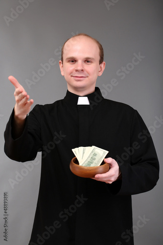 Photo: Young pastor with money on gray background Young pastor with money on gray background