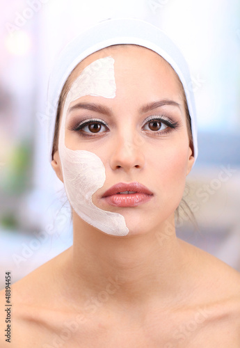Photo: Young woman with clay facial mask, on bright background Young woman with clay facial mask, on bright background