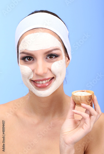 Photo: Young woman with clay facial mask, on blue background Young woman with clay facial mask, on blue background