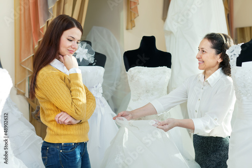 Photo: saleswoman helps girl chooses white bridal gown saleswoman helps girl chooses white bridal gown