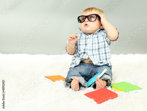 Photo: Little boy with multicolor books, on white carpet Little boy with multicolor books, on white carpet