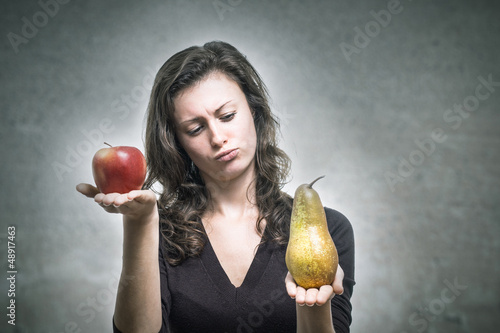 Photo: Junge Frau vergleicht Apfel und Birne Junge Frau vergleicht Apfel und Birne