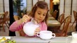Little girl takes jug with milk and pours it in plate at