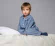 Disappointed little boy in blue pyjamas on bed