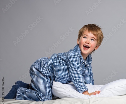 Photo: Playful little boy wearing blue pyjamas in bed Playful little boy wearing blue pyjamas in bed