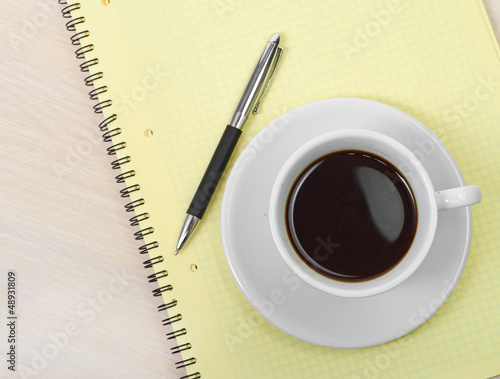 Photo: Coffee cup with note book on table Coffee cup with note book on table