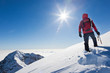 Mountaineer reaches the top of a snowy mountain in a sunny winte