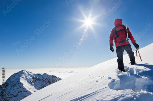 Photo: Mountaineer reaches the top of a snowy mountain in a sunny winte Mountaineer reaches the top of a snowy mountain in a sunny winte