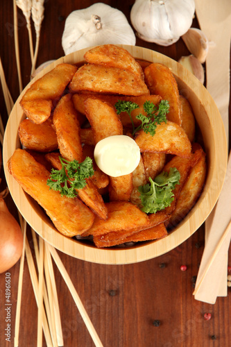 Photo: Appetizing village potatoes in bowl on wooden table close-up Appetizing village potatoes in bowl on wooden table close-up