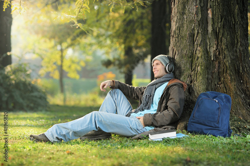 Photo: A male student relaxing and listening music seated in the park A male student relaxing and listening music seated in the park