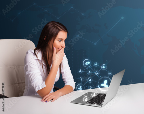 Photo: Young lady sitting at desk and typing on laptop with social netw Young lady sitting at desk and typing on laptop with social netw