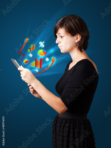 Photo: Young woman looking at modern tablet with abstract lights and va Young woman looking at modern tablet with abstract lights and va