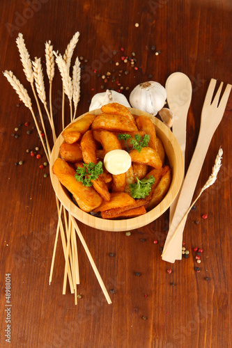 Photo: Appetizing village potatoes in bowl on wooden table close-up Appetizing village potatoes in bowl on wooden table close-up