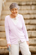 happy elderly lady standing by stairway with cane