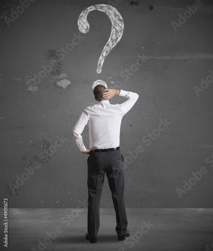 Photo: Confused businessman looking at question mark Confused businessman looking at question mark