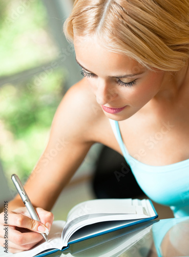 Photo: Young woman studying with notebook, indoors Young woman studying with notebook, indoors