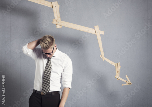 Photo: Disappointed businessman in front of graph pointing down. Disappointed businessman in front of graph pointing down.