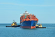 Tugboat assisting container cargo ship to harbor quayside