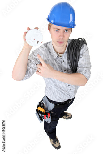 Photo: An electrician holding a fire alarm. An electrician holding a fire alarm.