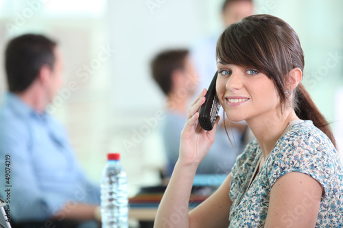 Photo: Woman with mobile phone colleagues sat in background Woman with mobile phone colleagues sat in background