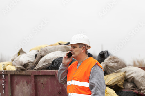 Photo: Worker with cell phone near garbage and container Worker with cell phone near garbage and container