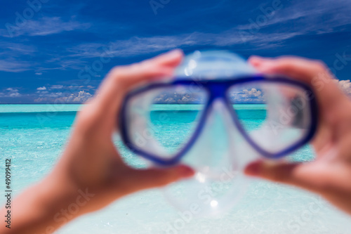 Photo: Hand holding snorkel goggles against beach and sky Hand holding snorkel goggles against beach and sky