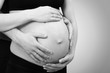 close-up of a pregnant belly with parents hands in black and whi