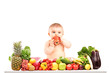 Cute baby boy sitting on a table with fruits and vegetables and