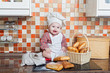 Foto: Baby cook with bread and steering-wheels sits on a kitchen table Baby cook with bread and steering-wheels sits on a kitchen table