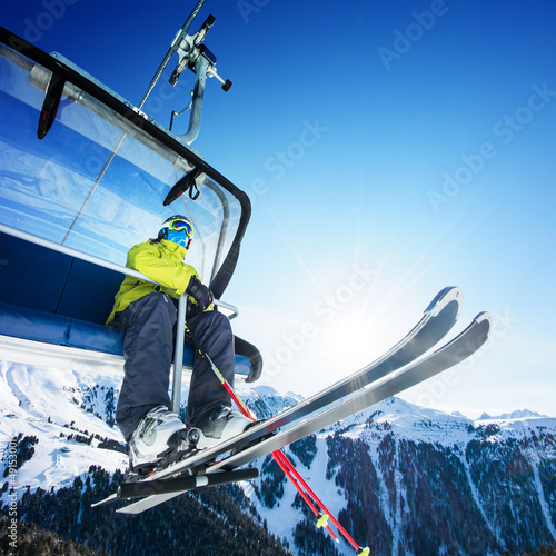 Photo: Skier siting on ski-lift - lift at sunny day and mountain Skier siting on ski-lift - lift at sunny day and mountain