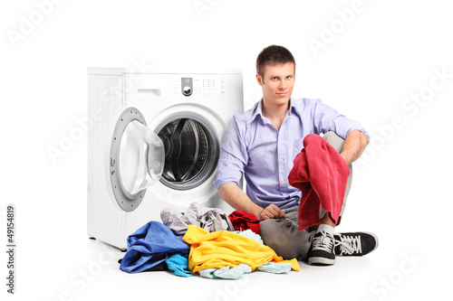 Photo: A young male sitting next to a washing machine A young male sitting next to a washing machine