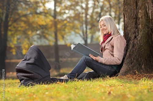 Photo: Young mother sitting in a park and reading a story to her baby Young mother sitting in a park and reading a story to her baby