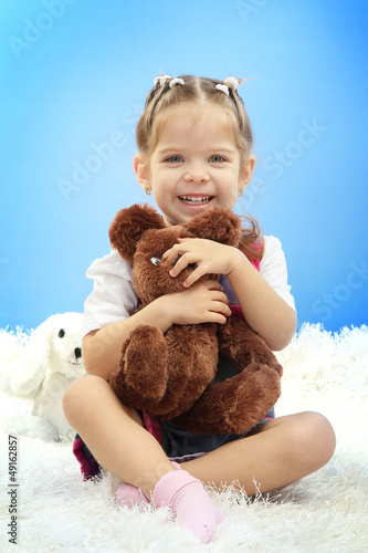 Photo: cute little girl playing with toy bear, on blue background cute little girl playing with toy bear, on blue background