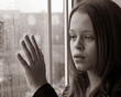A young girl gazing through a window with her hand raised