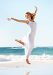 Photo: Happy young woman in white jumping in the air with the ocean beh Happy young woman in white jumping in the air with the ocean beh