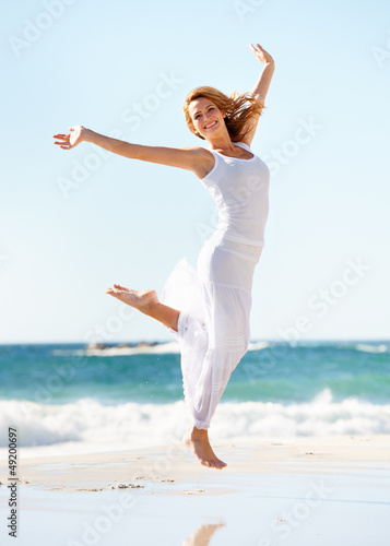 Photo: Happy young woman in white jumping in the air with the ocean beh Happy young woman in white jumping in the air with the ocean beh