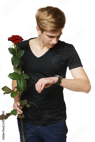 Photo: Young man holding red rose and looking at his wirstwatch Young man holding red rose and looking at his wirstwatch