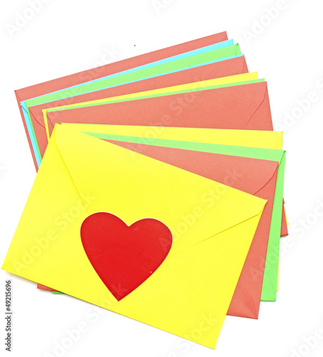 Photo: A red heart on pile colorful envelopes over white background A red heart on pile colorful envelopes over white background