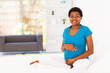 pregnant african woman sitting on bed at home
