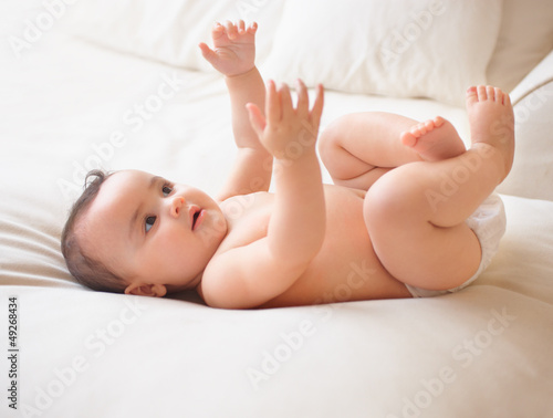 Photo: Shot of a cute baby reaching upwards while lying on a bed Shot of a cute baby reaching upwards while lying on a bed