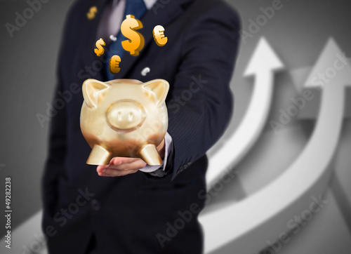 Photo: Businessman holding a gold piggy bank with currencies Businessman holding a gold piggy bank with currencies