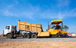 Tip truck unloading fresh asphalt from body into tracked paver