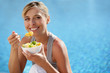 Woman eating fruit cocktail by swimming pool
