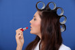 Woman with hair rollers applying lip-stick